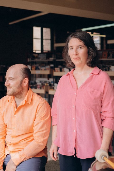 Une femme en chemise rose et un homme en chemise orange, dans une bibliothèque