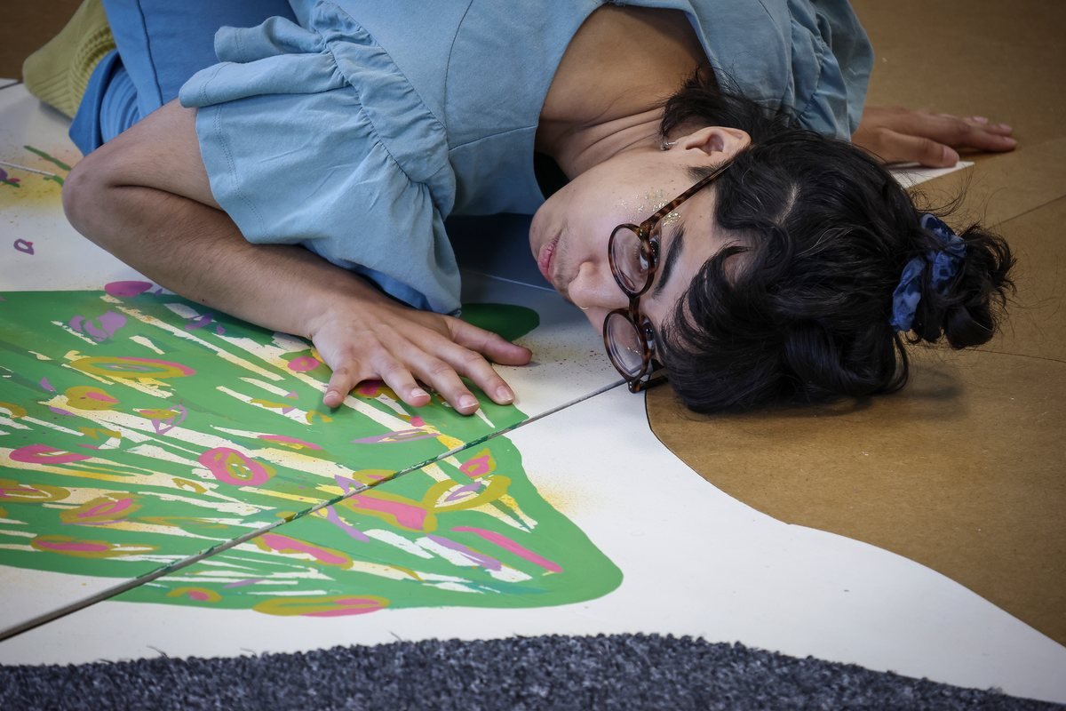 Une interprète allongée au sol, la tête posée sur la scénographie-puzzle de Peuplé·e·s